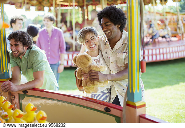 Smiling couple holding teddy bear next to fishing game in amusement park