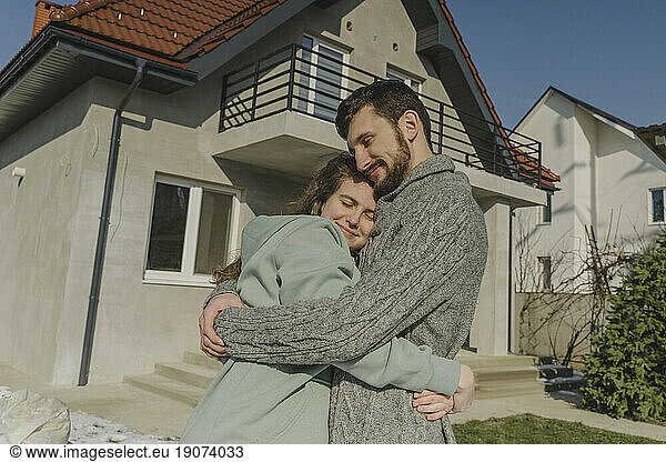 Smiling couple hugging in front of new house