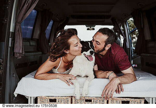 Smiling couple kissing dog while lying in camper trailer