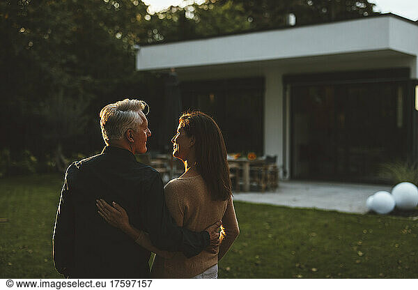 Smiling couple looking at each other in garden on sunset