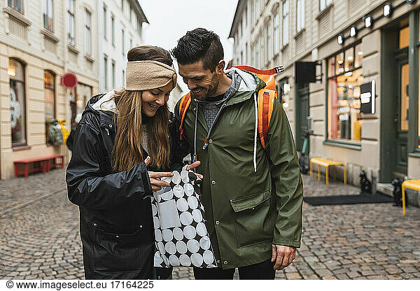 Smiling couple peeking in shopping bag while standing on street