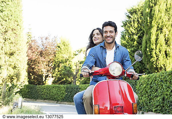 Smiling couple riding on motor scooter at park