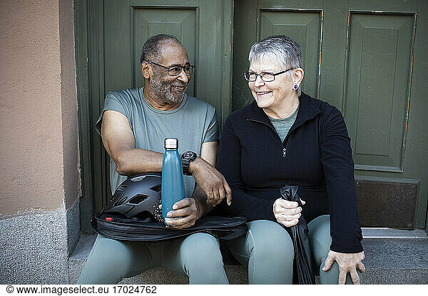 Smiling couple sitting against doorway of house