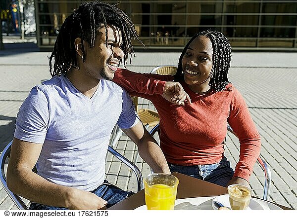 Smiling couple sitting at sidewalk cafe on sunny day