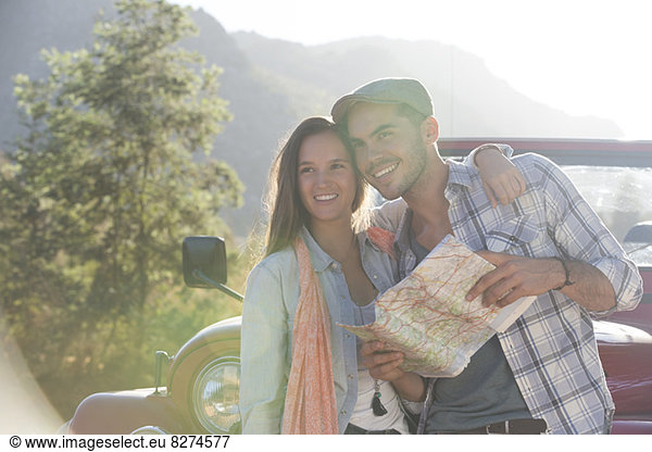 Smiling couple with map next to sport utility vehicle