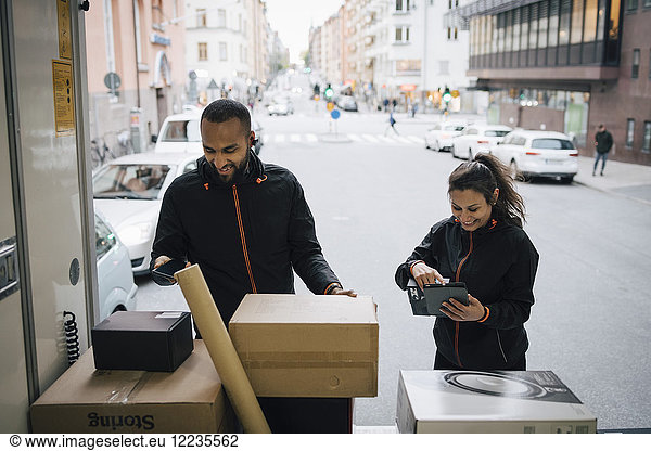 Smiling coworkers using technologies while examining packages in delivery van