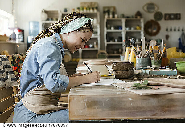 Smiling craftsperson drawing on sketch pad at art studio