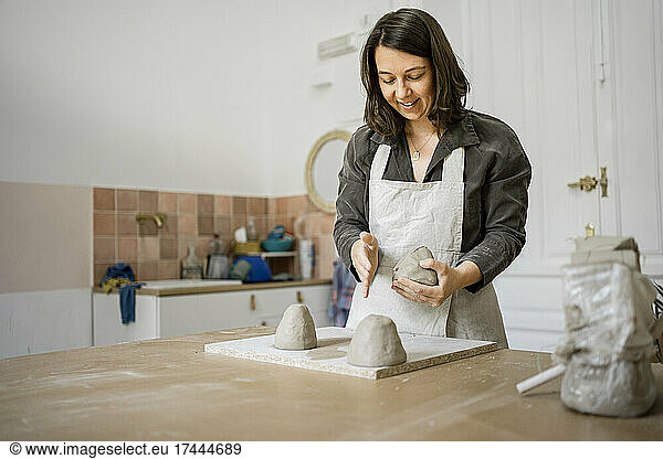 Smiling craftswoman making clay shape in workshop