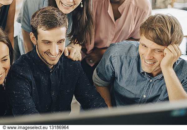 Smiling creative business people looking at computer monitor during meeting in office