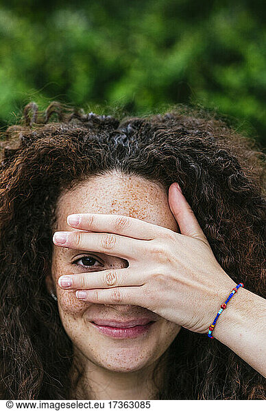Smiling curly haired woman peeking through fingers