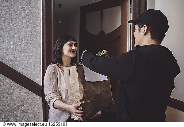 Smiling customer talking to delivery man while holding vegetable bag at doorstep