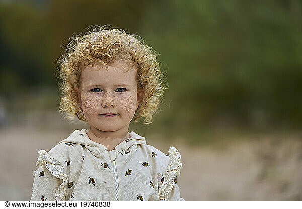Smiling cute blond girl with curly hair and freckles on face