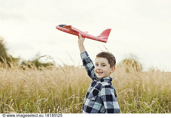 Smiling cute boy playing with model airplane in field