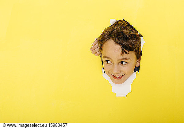 Smiling cute boy tearing yellow paper while looking away