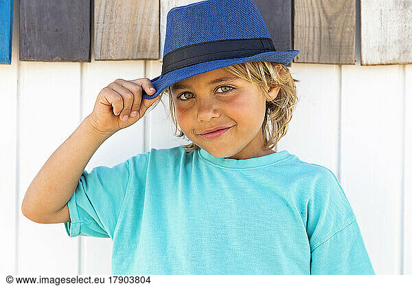 Smiling cute boy wearing hat in front of wooden wall