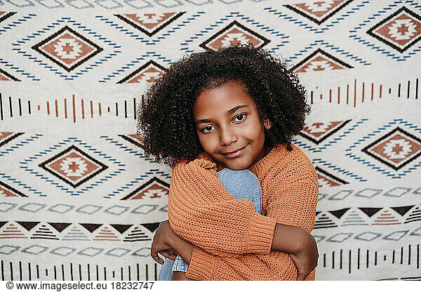 Smiling cute girl sitting in front of patterned backdrop