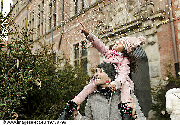 Smiling daughter gesturing and sitting on father's shoulders