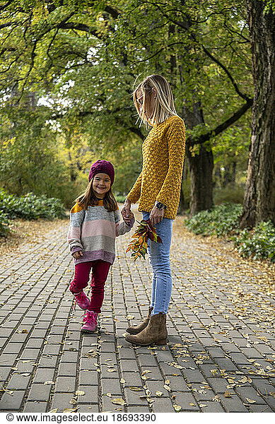 Smiling daughter holding mother's hand on footpath