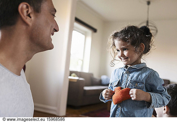 Smiling daughter showing stuffed heart shape to father at home