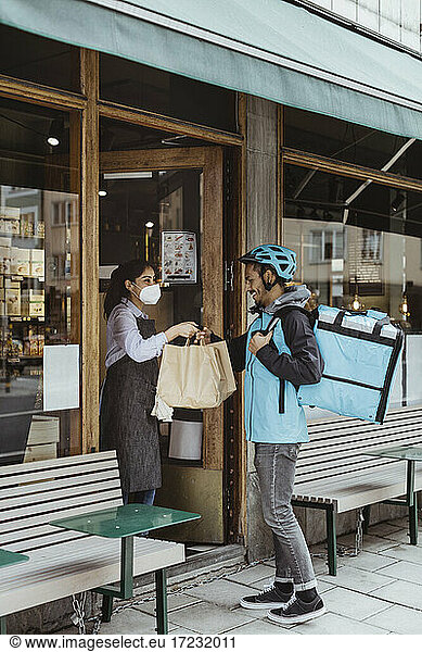 Smiling delivery man collecting order from sales woman at deli store during pandemic