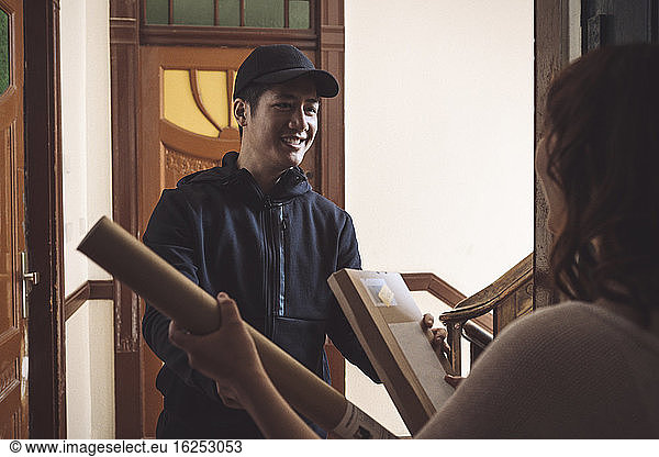 Smiling delivery man delivering package while talking to customer at doorstep