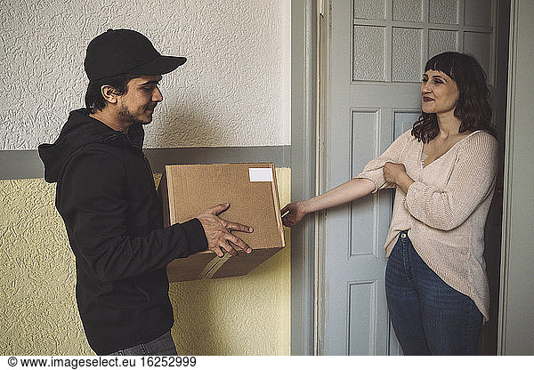 Smiling delivery man with package talking to customer at doorstep
