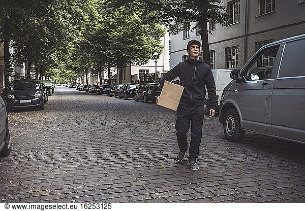 Smiling delivery man with package while walking on street in city