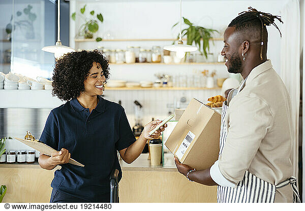 Smiling delivery woman scanning QR code from package in cafe