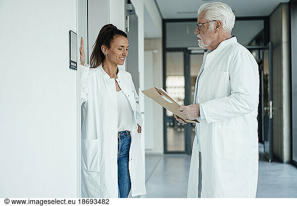 Smiling doctor discussing with senior colleague holding document in hospital