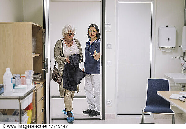 Smiling doctor gesturing to senior patient entering office at hospital