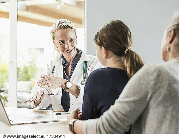 Smiling doctor giving advice to patient and woman at office