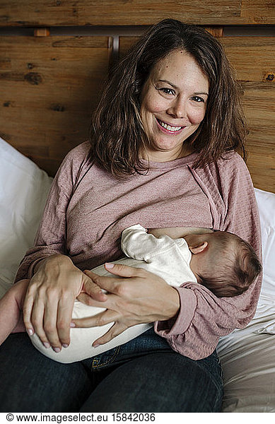 Smiling early-30â€™s mom wearing pink top breastfeeding newborn baby