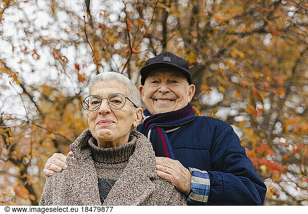 Smiling elderly couple under tree at autumn park