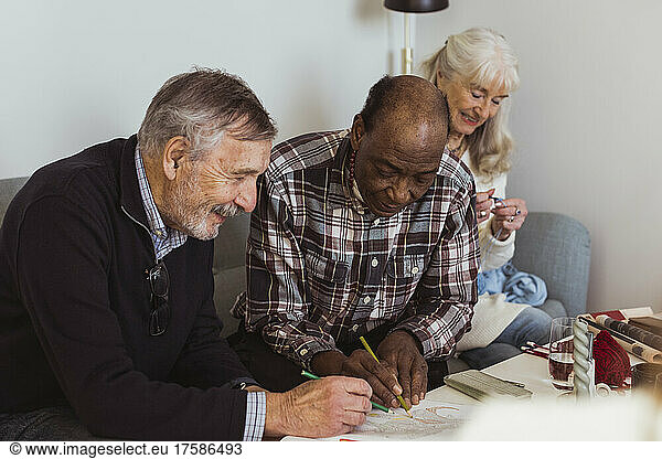Smiling elderly men drawing on paper by female friend at nursing home
