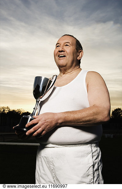 Smiling elderly men in sportswear  holding a silver trophy.