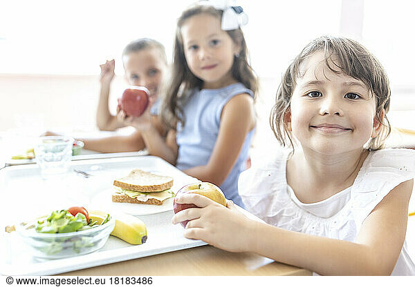Smiling elementary student with food tray on table at lunch break in cafeteria