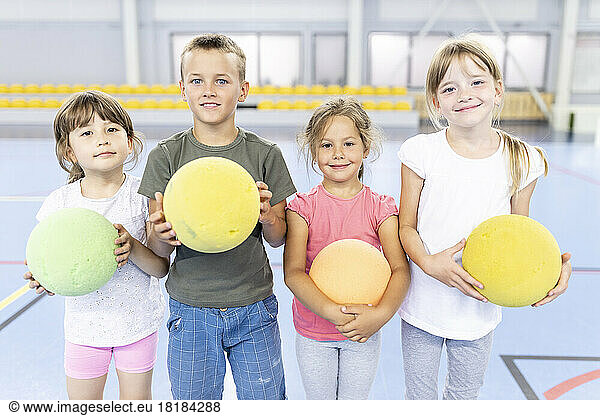 Smiling elementary students with ball standing side by side at school sports court