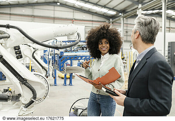 Smiling engineer holding folder discussing with colleague in factory