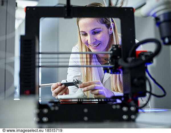 Smiling engineer holding vernier calliper operating 3D printing machine in laboratory