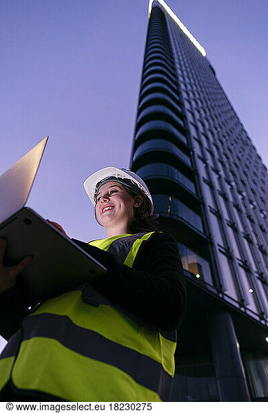 Smiling engineer using laptop in front of building at dusk