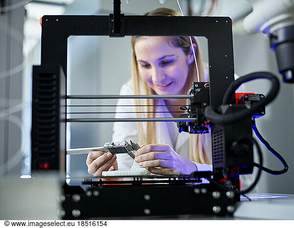 Smiling engineer with vernier calliper operating 3D printing machine