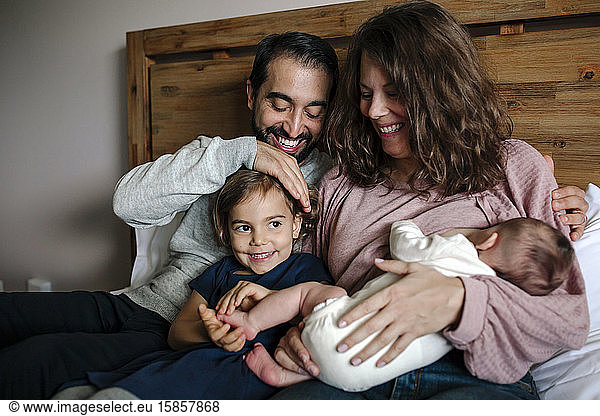 Smiling family cuddled together on bed as mother breastfeeds newborn