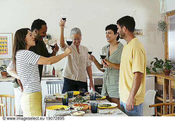 Smiling family raising toast standing near dining table in kitchen
