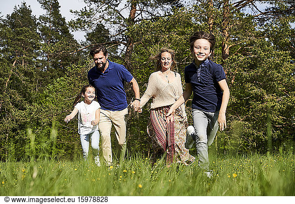 Smiling family running on grass against trees during sunny day