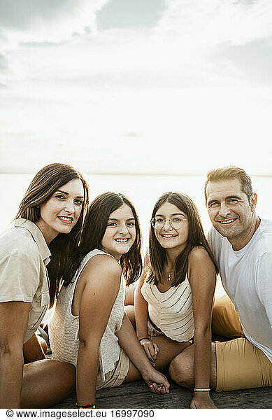 Smiling family sitting on jetty against sky
