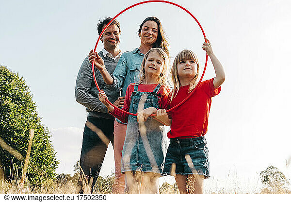 Smiling family with hula hoop in park on sunny day