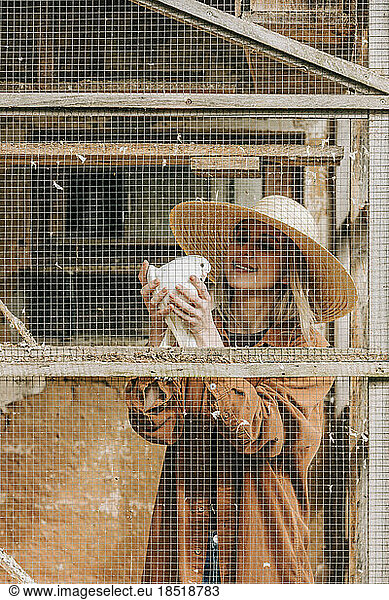 Smiling farmer holding bird standing in dovecote