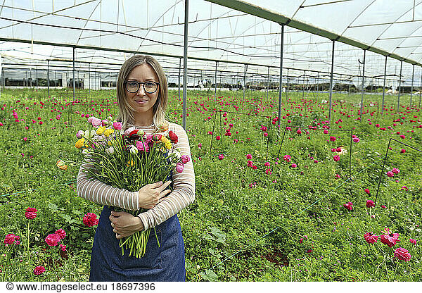 Smiling farmer holding bunch of flowers standing in greenhouse