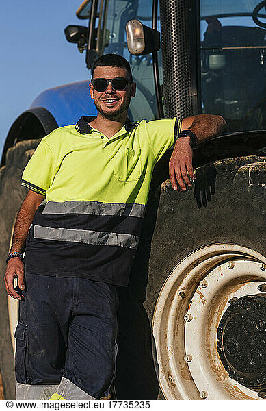 Smiling farmer wearing sunglasses standing by tractor