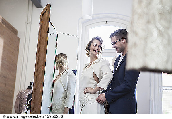 Smiling fashion designer and bride fitting dress in studio